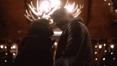a man and a woman are looking at each other in front of a chandelier