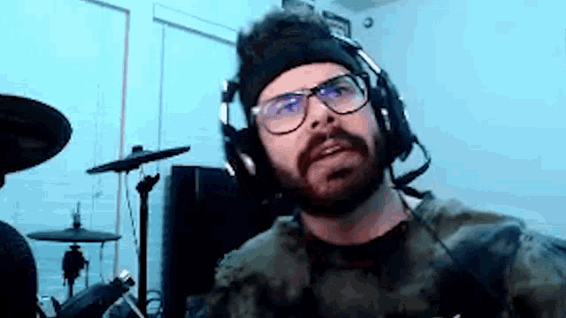 a man with a beard and glasses is wearing headphones and a headband in front of a drum set .