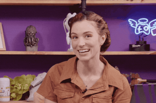 a woman smiles in front of a shelf with a neon sign that says angel