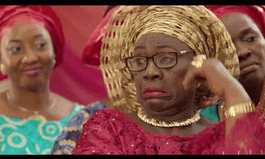 a woman wearing glasses and a gold necklace is making a funny face while sitting in a room with other women .