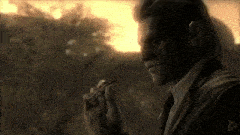 a man in a suit and tie is smoking a cigarette while talking on a cell phone .