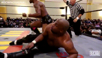 two men are wrestling in a ring with a referee in the background .