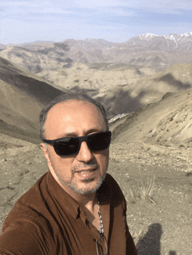 a man wearing sunglasses takes a selfie in front of mountains