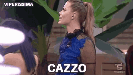 a woman in a blue dress is standing in front of a plant with the word cazzo on her back .
