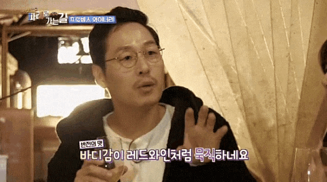 a man with glasses is holding a glass of wine with a foreign language subtitle