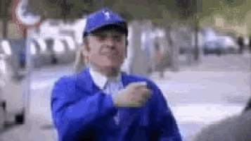 a man wearing a baseball cap and a blue jacket is standing on a sidewalk .