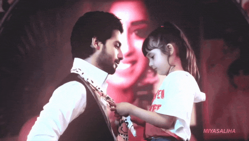 a little girl adjusts a man 's tie in front of a picture of a woman