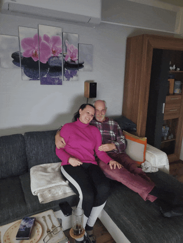 a man and a woman sit on a couch in front of a painting of flowers