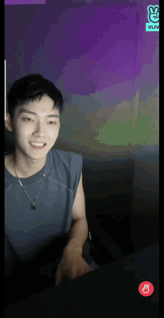 a young man is sitting in front of a purple wall with a vlive logo on it