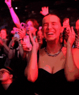 a woman in a black dress is smiling in front of a crowd