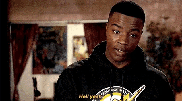 a man in a black hoodie is talking to another man in a room .