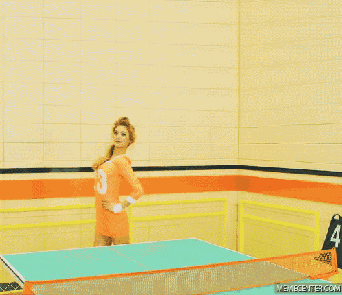 a woman in an orange shirt with the number 8 on it is standing next to a ping pong table