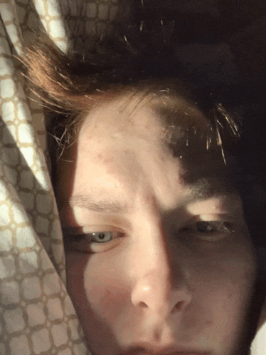 a close up of a person 's face with the sun shining through the curtain
