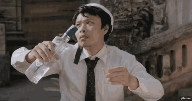 a man in a white shirt and tie is holding a bottle of water and a glass .