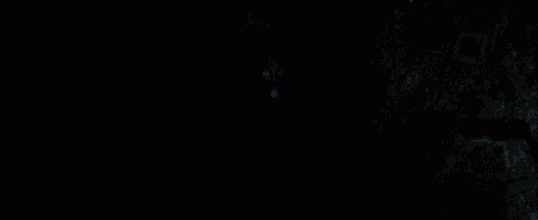 a man with black paint on his face is making a surprised face with his hands outstretched in the dark .