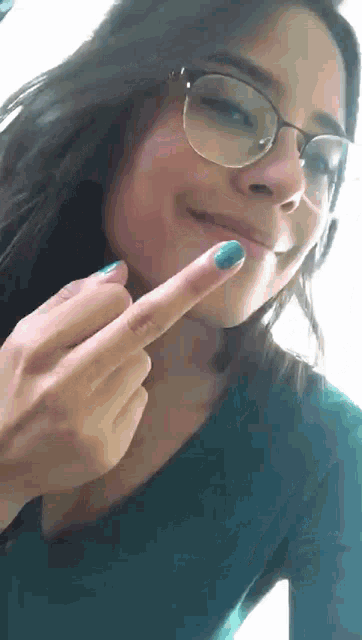 a woman wearing glasses and blue nail polish is pointing at her face