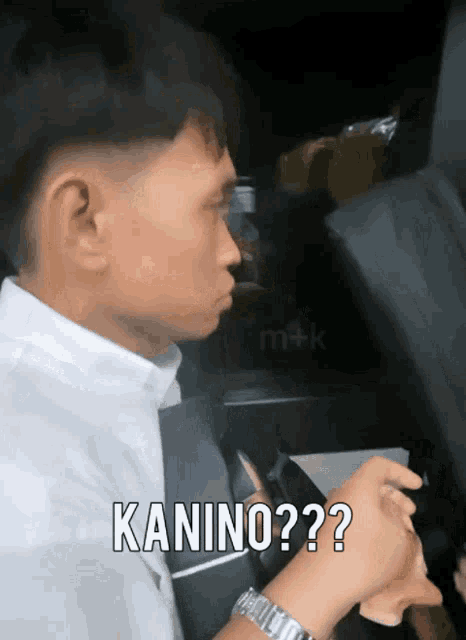 a man in a white shirt and black tie is driving a car and says kanino??
