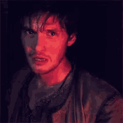 a close up of a man 's face in a dark room with a red light behind him