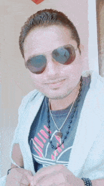 a man wearing sunglasses and a necklace has a pink adidas shirt on