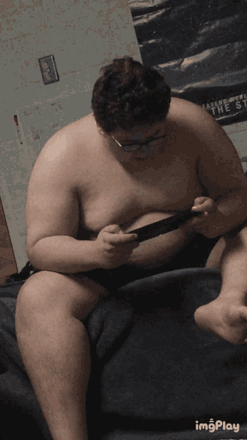 a shirtless man is sitting on a bed with a poster on the wall that says leading from the front