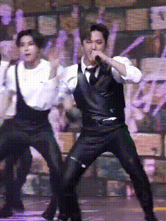 a man in a suit and tie is singing into a microphone while another man stands behind him .