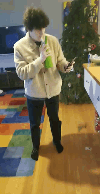 a person standing in front of a christmas tree with a green bottle in their hand