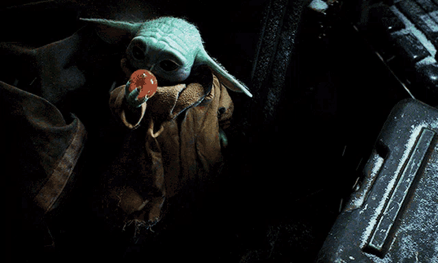 a baby yoda holding a red ball in his hand in the dark
