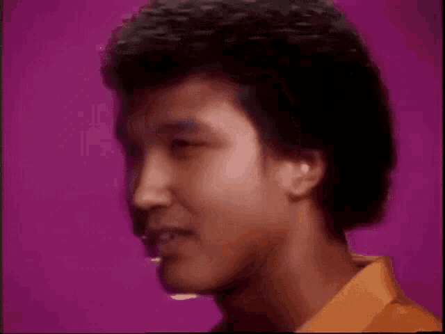 a close up of a man 's face with a purple background and a yellow shirt .