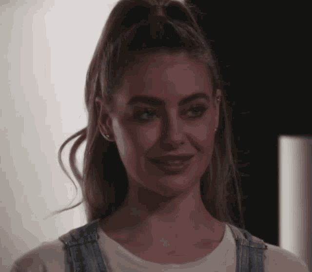 a woman in overalls and a white shirt smiles