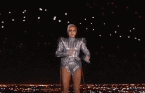 a woman in a silver outfit is dancing on a stage in front of a city at night .