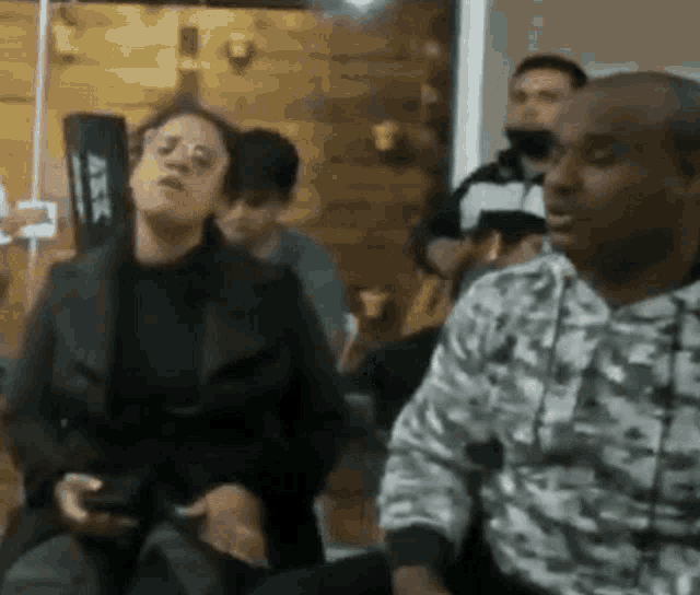 a group of people are sitting in a room with a man in a camouflage shirt .