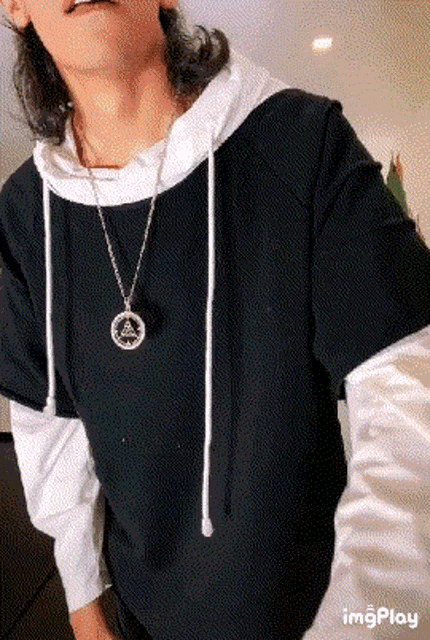 a man is wearing a black hoodie and a white shirt with a necklace .