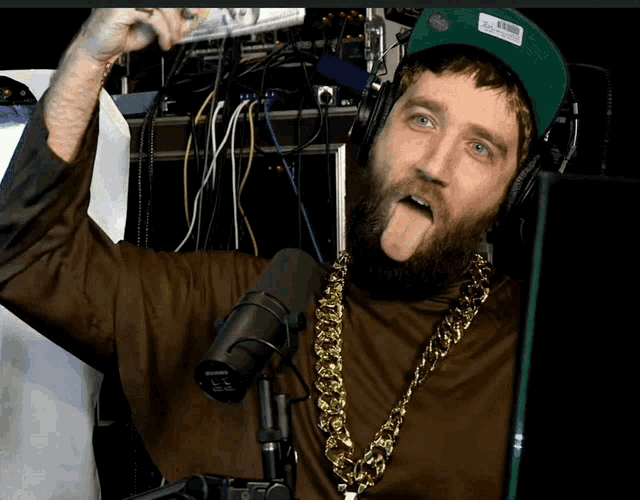 a man with a beard wearing headphones and a shure microphone sticking out his tongue