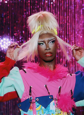 a woman in a pink and blue outfit holds her blonde hair