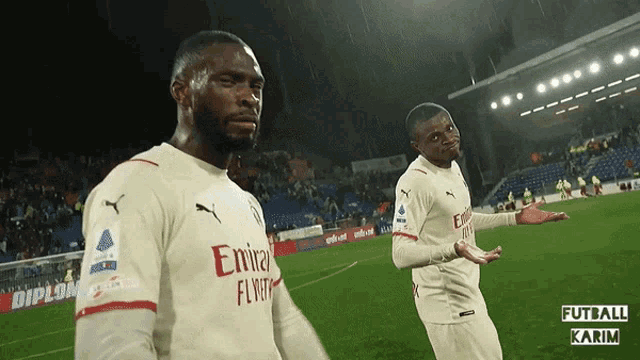 two soccer players wearing emirates fly emirates jerseys are standing on a field