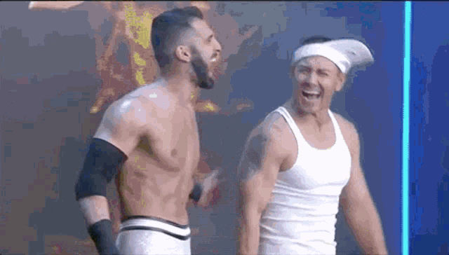 two shirtless men are standing next to each other and laughing . one of the men is wearing a headband .