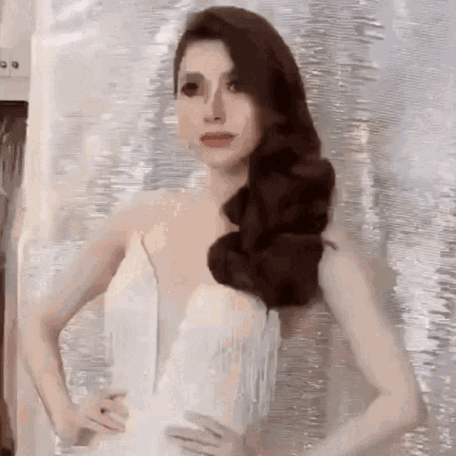 a woman in a white dress with fringe is standing with her hands on her hips and looking at the camera .