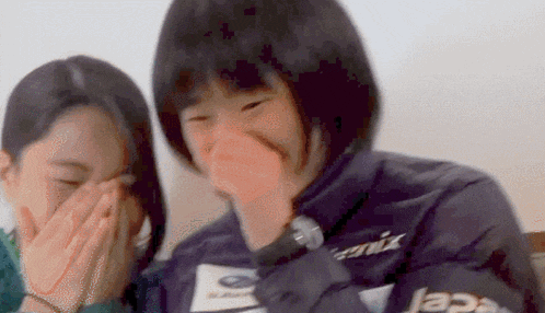 two young girls are covering their mouths with their hands while laughing .
