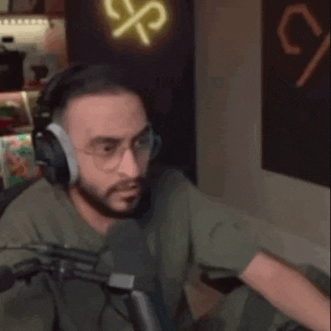 a man is wearing headphones and glasses while sitting in front of a microphone .