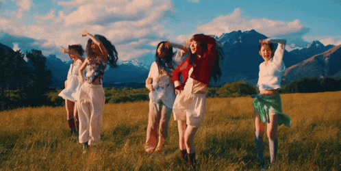a group of young women dancing in a field with mountains in the background