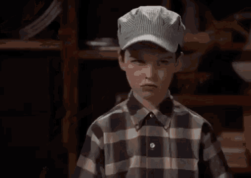 a young boy wearing a striped hat and a plaid shirt is making a funny face .
