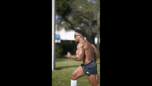 a shirtless man is running in a park wearing sunglasses