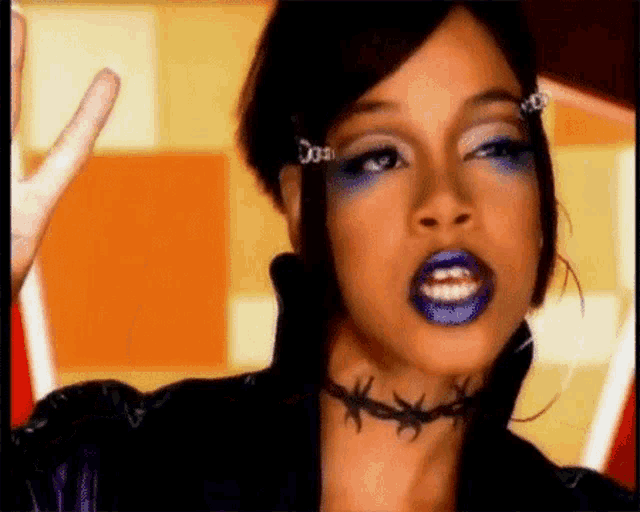 a woman wearing purple lipstick and barbed wire choker is making a peace sign .