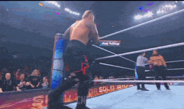 a man is kneeling in a wrestling ring while a referee stands behind him .