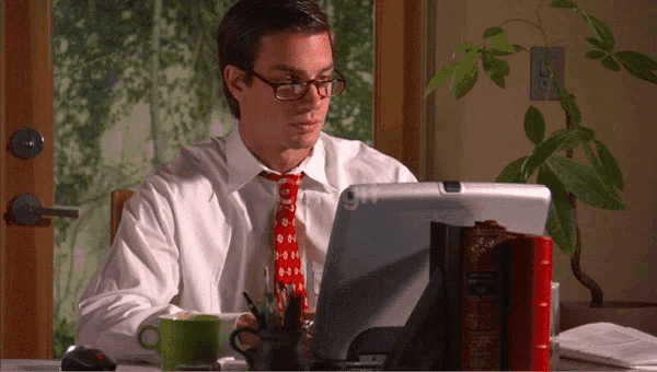 a man wearing glasses sits at a desk using a tablet