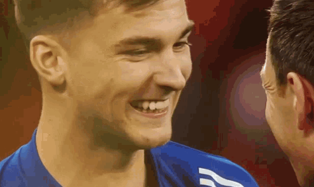 a man wearing a blue shirt with the letter a on it smiles