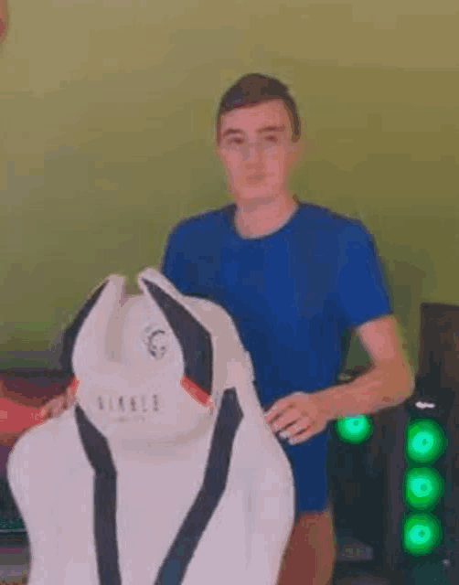 a man in a blue shirt is holding a white gaming chair in his hands .