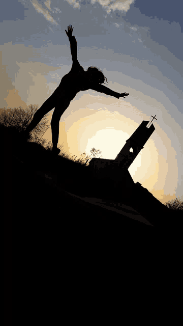 a silhouette of a person with their arms outstretched with a church in the background