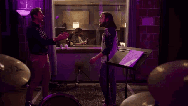 two men are standing in front of a microphone in a recording studio .