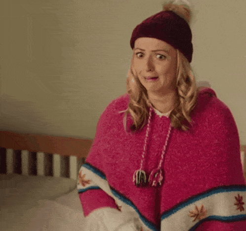 a woman wearing a pink poncho and a hat is making a funny face .
